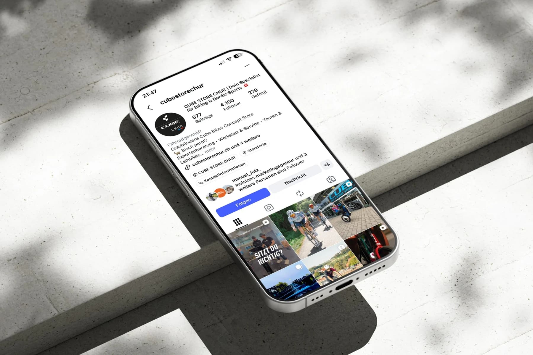 Instagram-Auftritt des CUBE STORE CHUR als Handy-Mockup: ein Handy liegt schräg auf hellem Beton, auf dem Bildschirm das Profil @cubestorechur mit 677 Beiträgen und 4.100 Followern und dem Raster der Beiträge